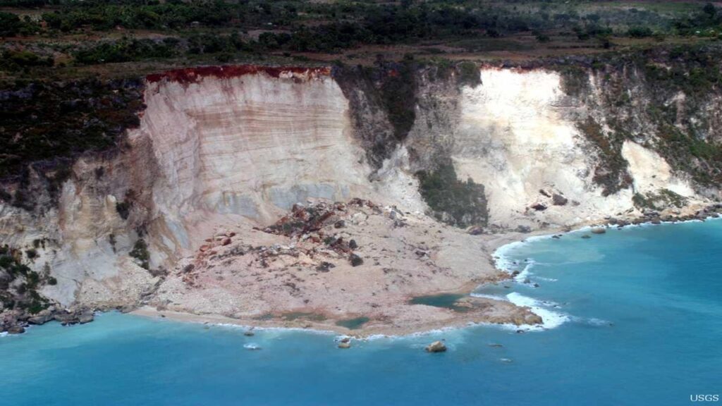 Coastal landslides, cream cliff material falling into blue ocean from grey cliff exposing cream slope