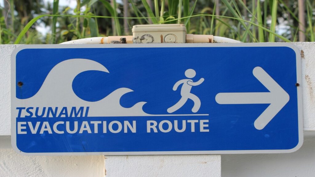 Blue and white sign board reading tsunamis evacuation route and icon of man running in front of tsunami waves